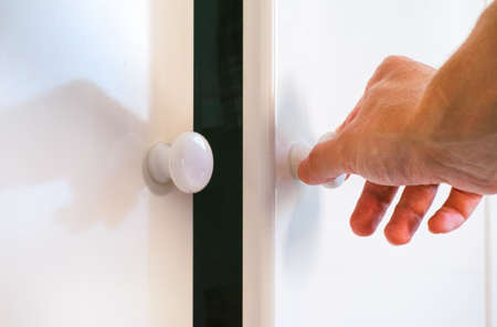 Person hand opening door of white wardrobe. Close-up.