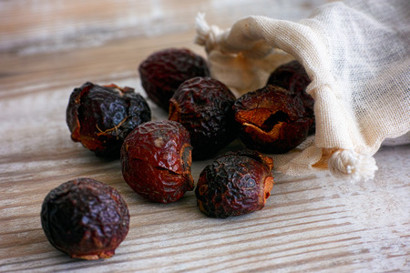 Soap nuts spilling from bag on wooden background. Close-up.