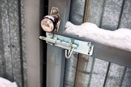 Metal door with door knob and bolt covered snow. Close-up.