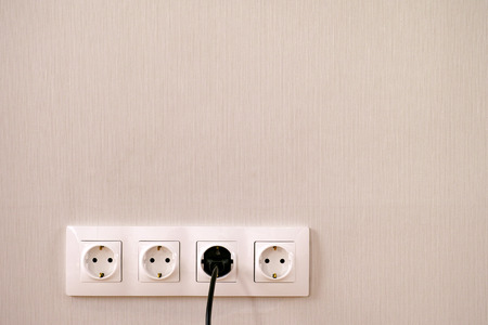 Four power sockets, black lead and plug on the wall. Close-up.