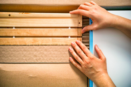 Woman hands unpacking cardboard box with parts of  furniture. Close-up.