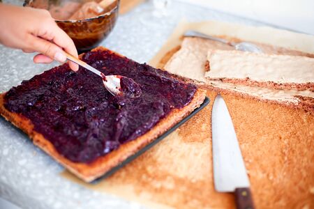 Woman making cake. Person hand with spoon spreads jam on sponge cake on domestic kitchen.の写真素材