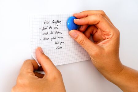 Woman hands attaching a note on the fridge. Dear daughter, feed the cat, wash the dishes, clean your room. Love you, Mum.の写真素材