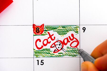 Woman fingers with red pen writing reminder Cat Day in calendar. Close-up.の写真素材