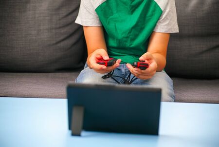 Kid with two gamepads playing video game console indoors.