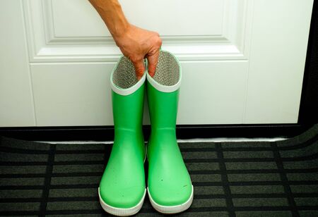 Person hand picking up pair of green child rubber boots near the door.