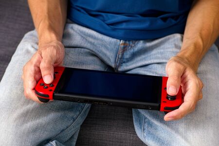 Tambov, Russian Federation - June 22, 2019 Man sitting on sofa and playing Nintendo Switch video game console.のeditorial素材