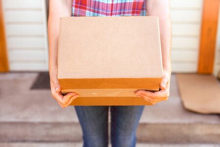Woman with cardboard box stands near her house.の写真素材