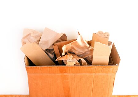 Cardboard box with crumpled paper and cardboard pieces against white wall. Close-up.