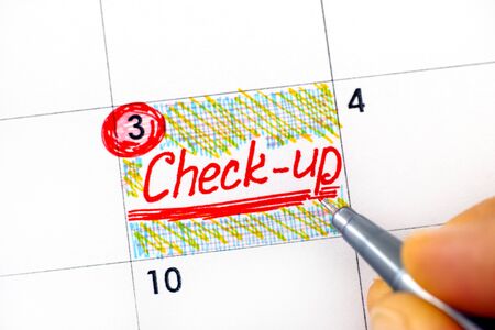 Woman fingers with pen writing reminder Check-up in calendar. Close-up.