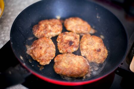Homemade cutlets in frying pan cooking on induction hob in domestic kitchen. Close up.の写真素材