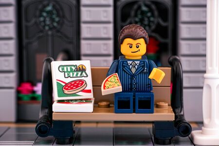Tambov, Russian Federation - October 16, 2019 Lego businessman eating pizza on the bench outside....