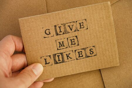 Woman hand holding cardboard card with words Give Me Likes made by black alphabet stamps against...