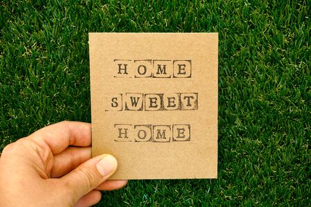 Cardboard with words Home sweet home in woman hand against green grass background.の写真素材