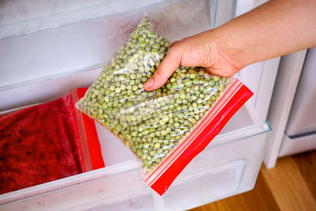 Woman hand taking out homemade packing of green peas in the freezerの写真素材