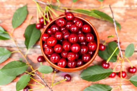 Bowl with ripe red cherries and cherry tree twigs on wooden background.の写真素材