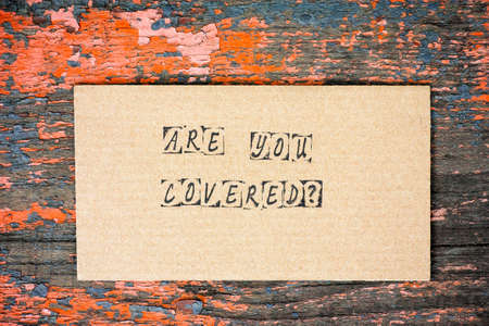 Cardboard with words Are You Covered? made by black alphabet stamps. Old wooden background.の写真素材