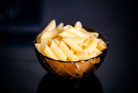 Cooked gluten free pasta penne in the glass bowl. Black background.