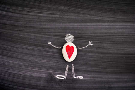 Pebble with red heart inside chalk drawing of man on black board.