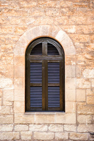 Arched window with closed shutters on yellow stone wallの写真素材