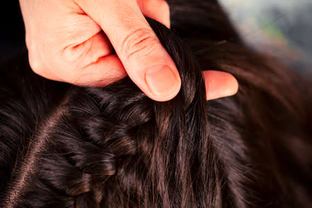 Woman hand braiding brunette girls long hair. Close-up