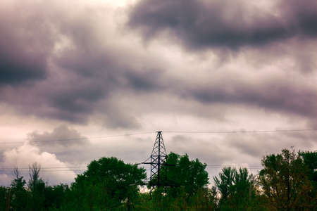Beautiful cloudy sky over transformer line tower and green treetops.