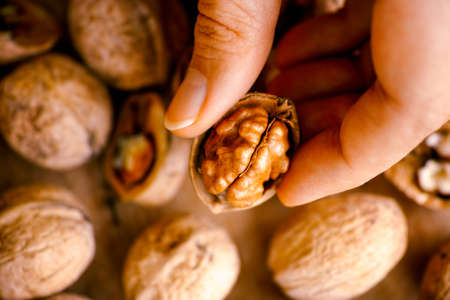 Woman hand with open walnut above walnuts on wooden background.