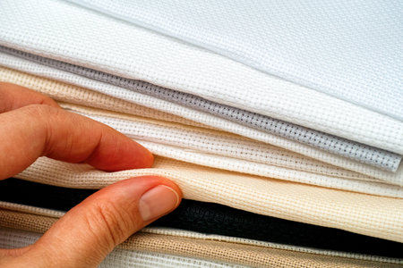 Woman hand taking beige canva from stack of colour cross stitch fabrics