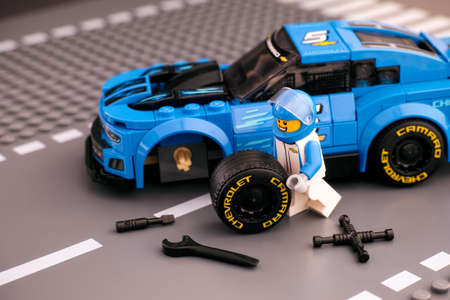 Tambov, Russian Federation - February 14, 2021 Lego driver minifigure fixing wheel of Chevrolet Camaro ZL1 race car by LEGO Speed Champions. Road baseplate background.のeditorial素材