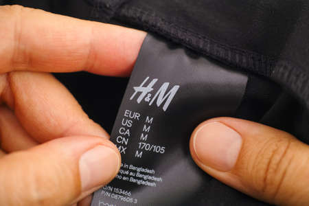 Tambov, Russian Federation - June 08, 2021 Woman hands holding H&M female clothes label  with size conversions in different countries.のeditorial素材