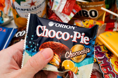 Tambov, Russian Federation - October 30, 2020 Person hand with Orion Choco Pie Chocochip and Orange snack cake. A lot of sweet snack on background.のeditorial素材