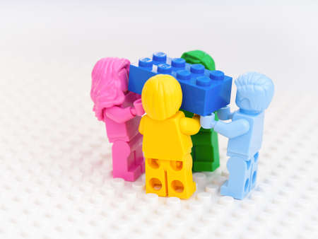 Tambov, Russian Federation - October 17, 2021 Four monochrome Lego minifigures carrying a blue Lego brick. White background. Studio shot.のeditorial素材