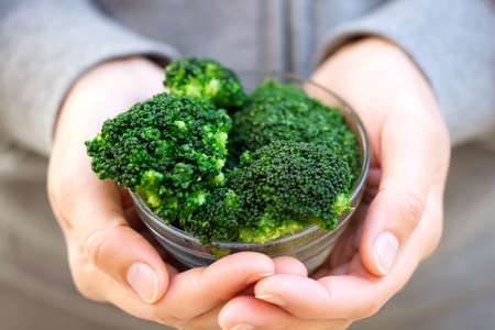 Cooked broccoli in a bowl in woman's handsの写真素材