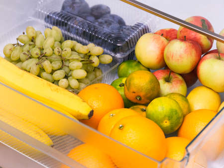 A fridge drawer full of fruits (oranges, tangerines, grapes, bananas, apples, plums).の写真素材