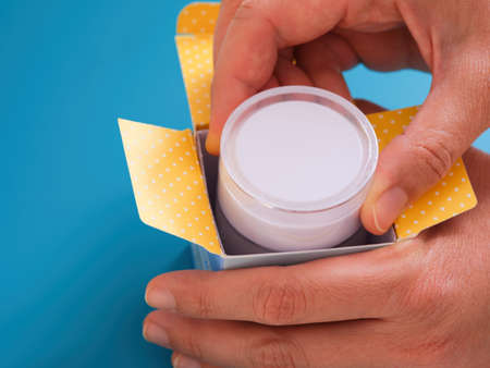 A woman taking face cream out of a box. Blue background.の写真素材