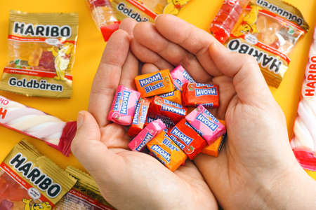 Tambov, Russian Federation - January 06, 2021 Woman palms full of Maoam Bloxx candies. There are some Haribo candies on yellow background.のeditorial素材