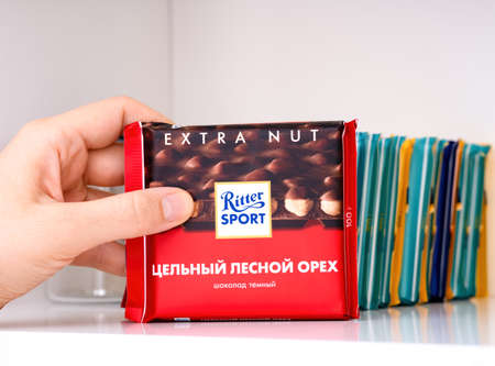 Tambov, Russian Federation - February 19, 2022 Woman hand taking Ritter Sport Hazelnut chocolate bar from stack on shelf of a kitchen cupboardのeditorial素材
