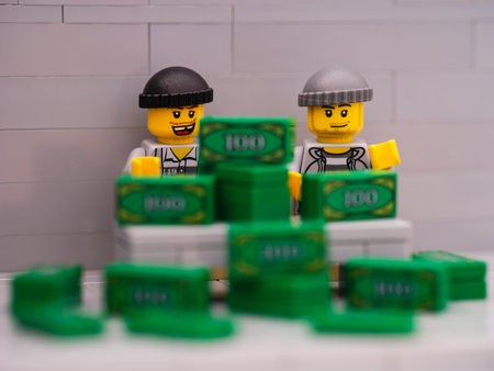 Tambov, Russian Federation - March 25, 2023 Two Lego thief minifigures sitting behind a desk with a pile of money on it.のeditorial素材