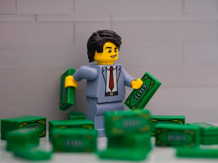 Tambov, Russian Federation - March 25, 2023 Lego businessman minifigure holding two Lego banknotes standing in a pile of money.のeditorial素材