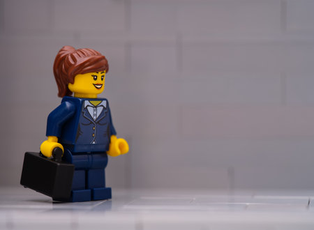 Tambov, Russian Federation - March 25, 2023 A Lego businesswoman minifigure with a black suitcase on a gray background.のeditorial素材