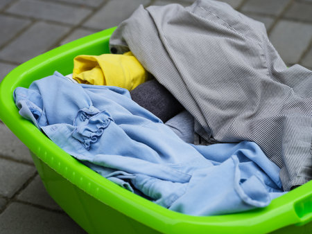Clean dried clothes laying in a green laundry basket outdoors. Close-upの写真素材