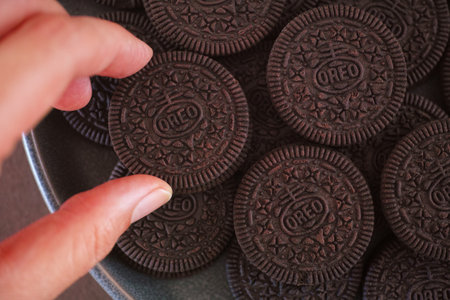 Tambov, Russian Federation - November 08, 2023 Woman taking Oreo cookie from a gray plate full of Oreo cookiesのeditorial素材