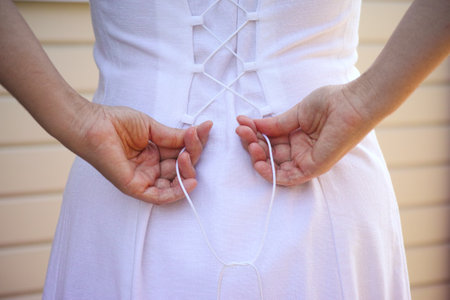 A girl tightening laces on the back of her white dress.の写真素材
