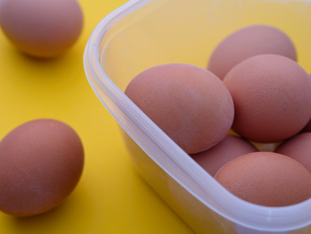 Plastic container with boiled eggs on a yellow background.