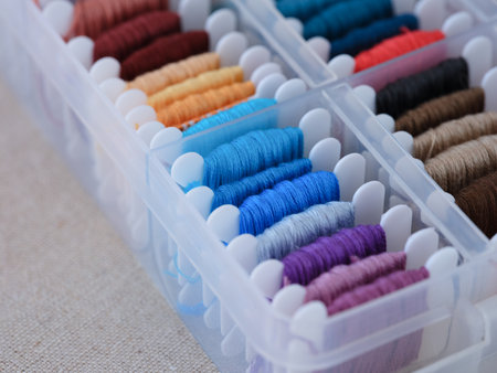 A close-up shot of a plastic sorting box full of bobbins with different colour embroidery threads on...