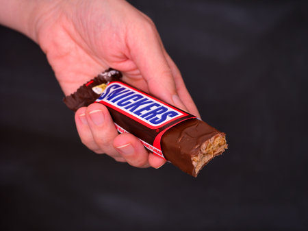 Tambov, Russian Federation - January 31, 2024 Woman hand with an open Snickers bar against a black background.のeditorial素材