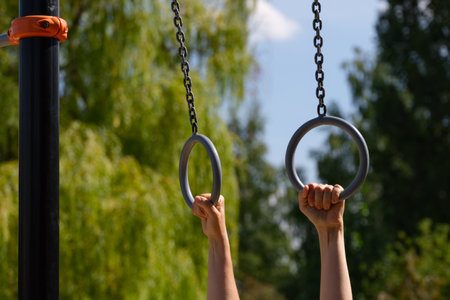 Person hands holding onto gymnastic rings outdoors.の写真素材