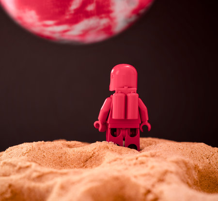 Red astronaut figure standing on sand on a planet and looking at another red planet. Back view.の写真素材