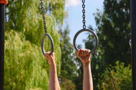 Person hands holding onto gymnastic rings outdoors. Close-up.の写真素材