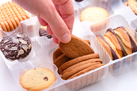 Woman hand taking cookie from plastic box with different kinds of cookies in it. Close-upの写真素材